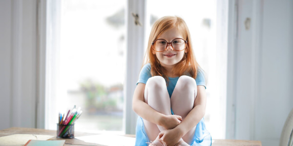 Little girl wearing glasses sitting smiling at the camera