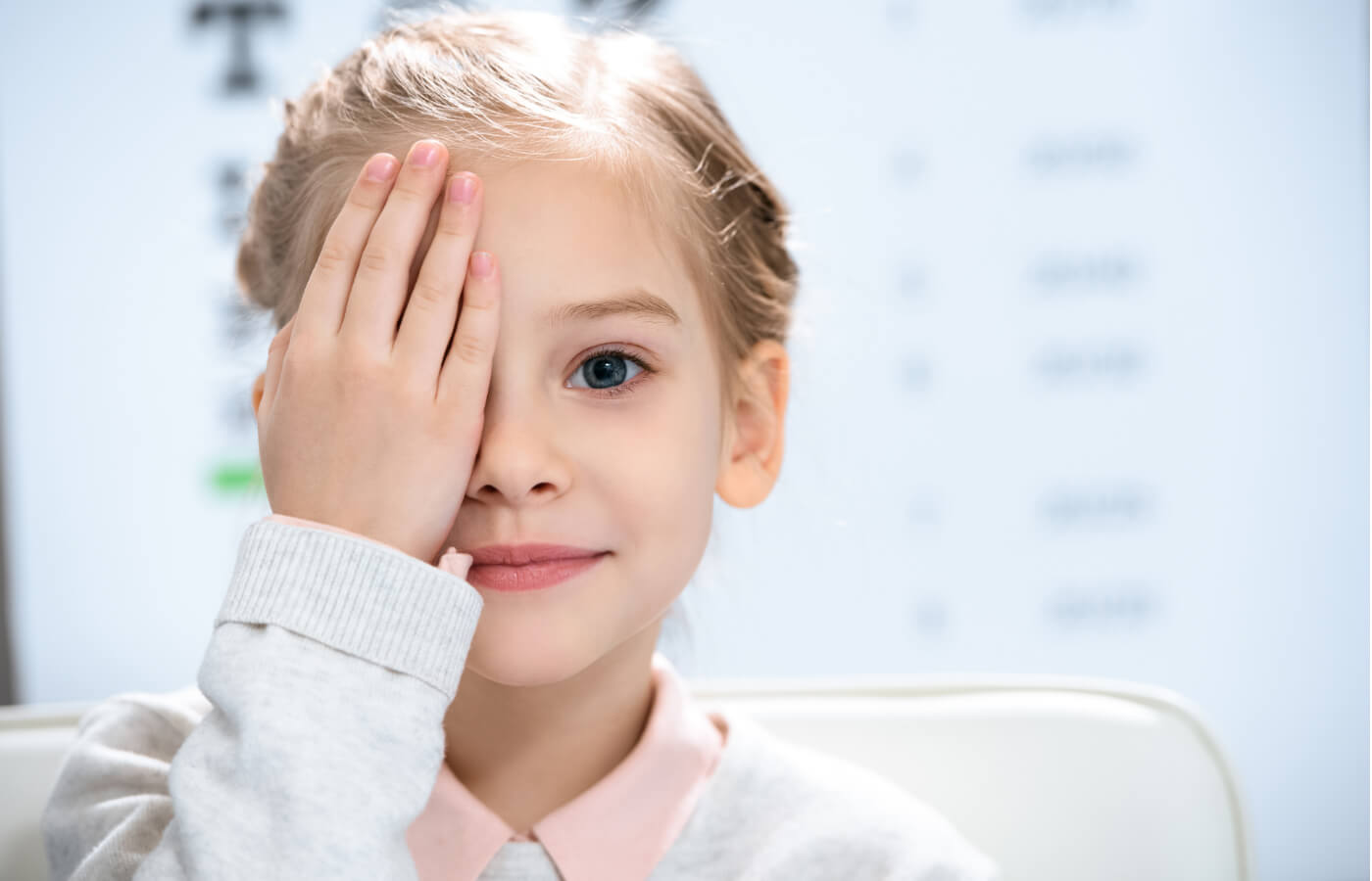 Young girl covering her right eye with her right hand.